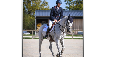 A rider in formal attire riding a gray horse in an outdoor arena.