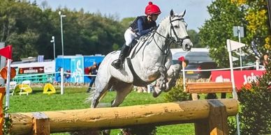 A rider on a white horse jumps over an obstacle at Blenheim Palace Horse Trials 2025.