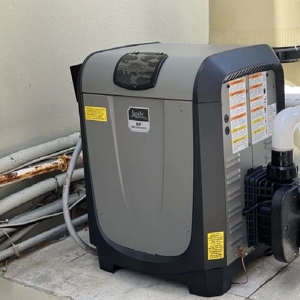 Outdoor pool heater unit installed beside a wall with piping.