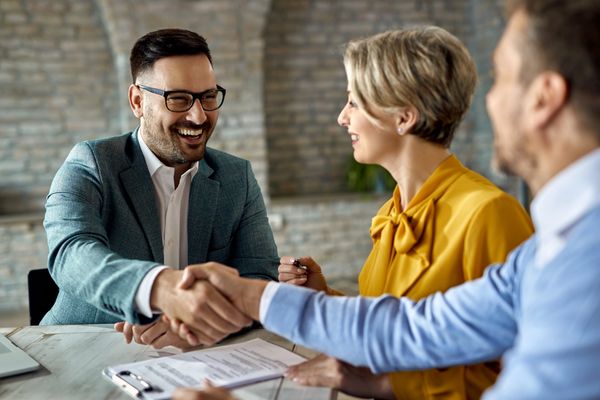 Three professionals engaged in a handshake over a table with documents in a modern