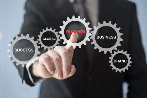 A businessman in a suit presses a gear labeled "Franchise,"