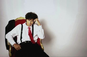 Man in white shirt with red tie sitting thoughtfully.