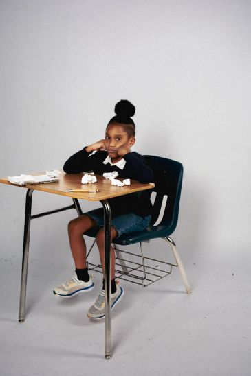 A girl looks bored sitting at a desk with crumpled paper.