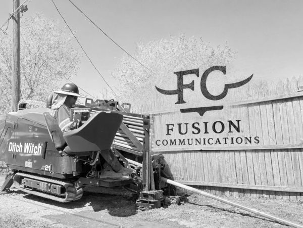 Worker operating heavy machinery near a fence with Fusion Communications logo.