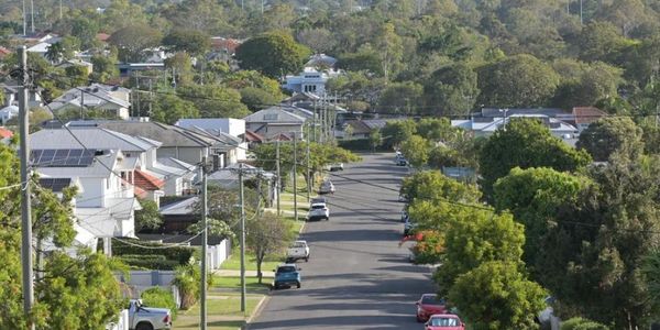 Suburban street with parked cars and city skyline in the distance.