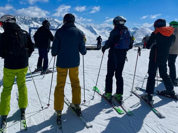 Group of males posing for a photo at the top of the mountain in their ski gear.