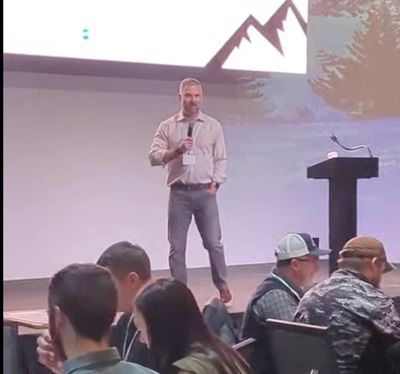 Man giving a presentation on stage with an audience seated.