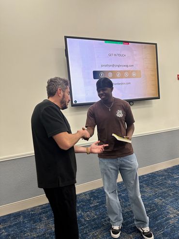 Professional guest speaker shaking an AMA student's hand and giving him a book at a meeting.