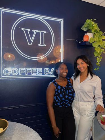 Two female members of the AMA board next to the VI Coffee Bar logo. The girl on the left is current