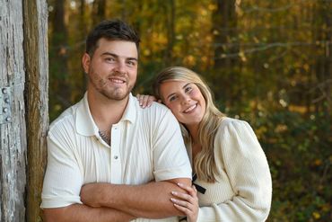 Smiling couple leaning against a tree in a forest during autumn.