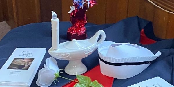 Memorial display with a candle, white rose, and booklets on a patriotic cloth.