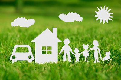 White paper cutouts of a house, car, family, and dog on green grass, with sun and clouds