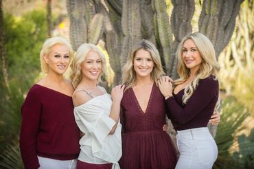 Four smiling women posing outdoors in coordinated burgundy and white outfits.