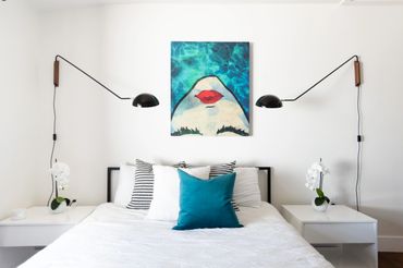 Modern bedroom with white bedding, teal pillow, and artistic shark painting.