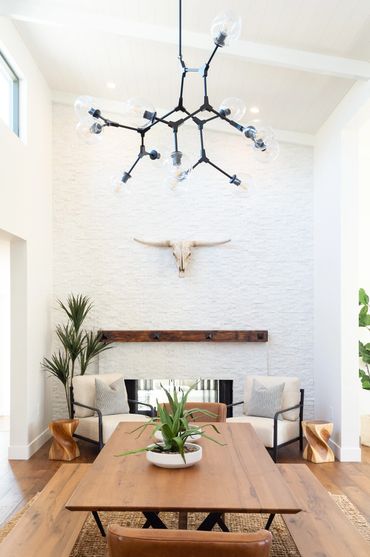 Modern dining room with wooden table, beige chairs, and decorative skull on white textured wall.