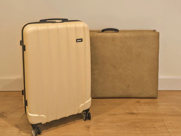 A beige suitcase with wheels and a large brown case on a wooden floor.