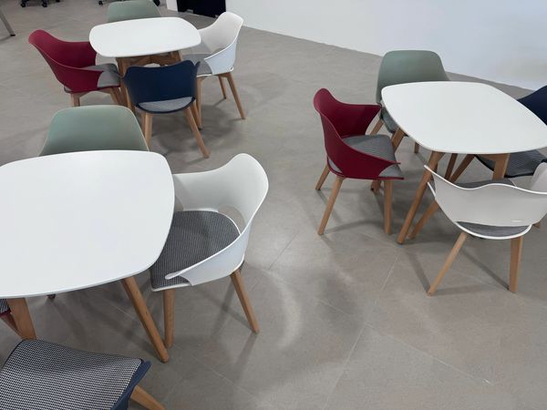 Modern white tables with colorful chairs in a minimalist room.