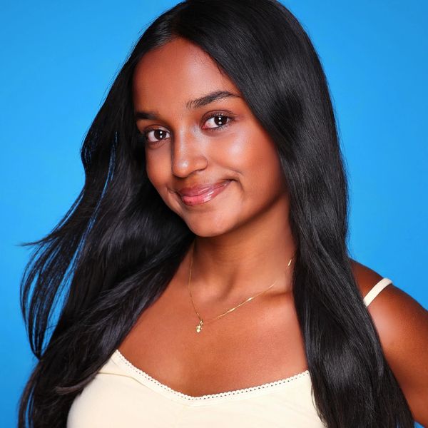 Young woman with long black hair smiling against blue background.