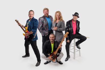 Group of five musicians posing with guitars and smiles.