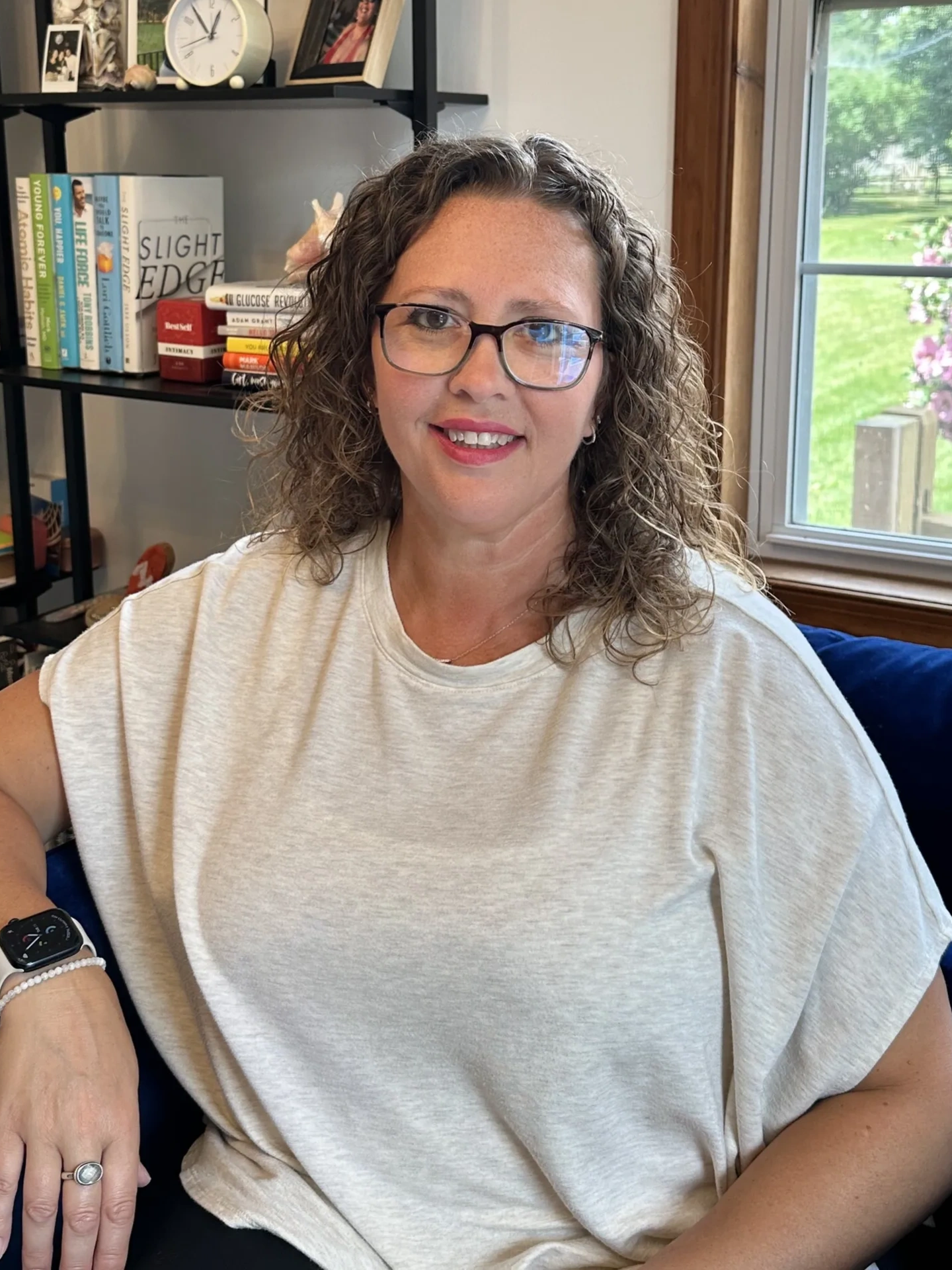 Naomi Kreske sitting in her blue chair with glasses on and smiling