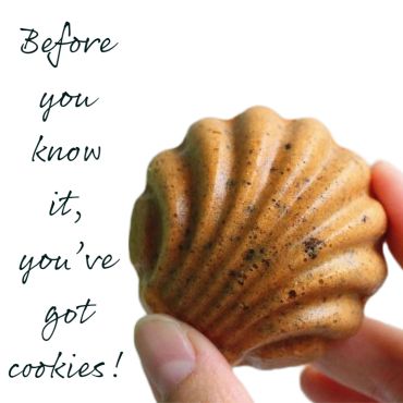 Hand holding a seashell-shaped cookie with text.