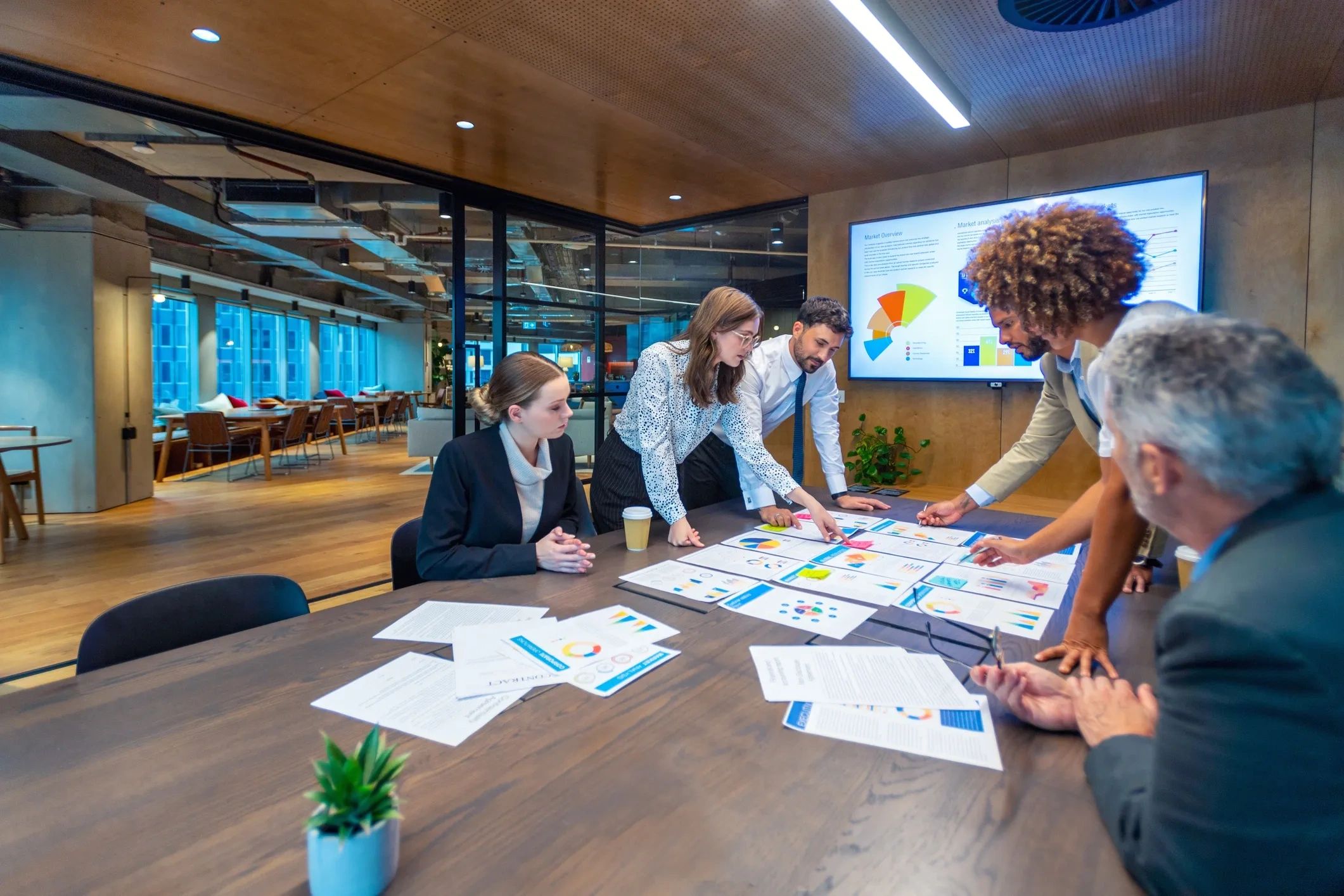 A team collaborates over charts and graphs in a modern office meeting room.