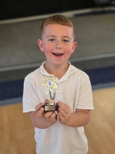 Young boy proudly holding a trophy and smiling.