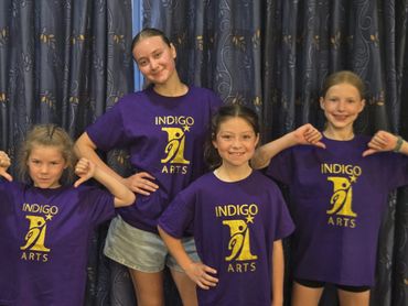 Four girls in purple Indigo Arts t-shirts posing in front of a curtain.