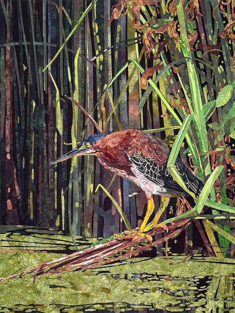 Fabric collage of a Green Heron emerging from shadowed foliage on a shoreline