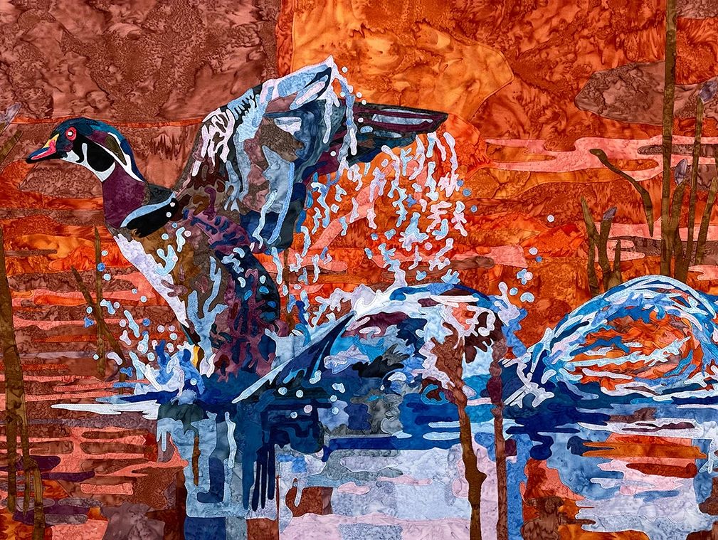 Fabric collage of a Wood Duck taking flight from the water at dawn