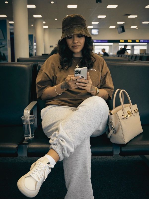 Woman in casual wear sitting at an airport, using her phone.
