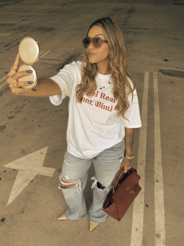 Woman taking a selfie in a parking lot wearing sunglasses and casual clothes.