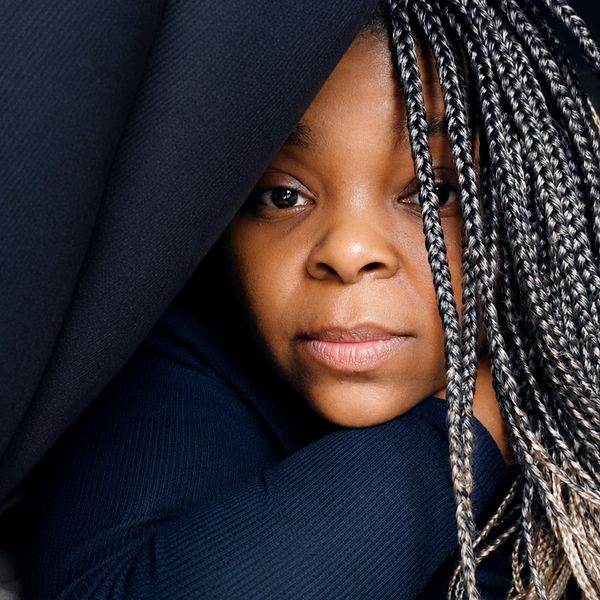 Close-up portrait of a woman with braided hair peeking from behind a dark fabric.