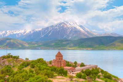 Ancient church by a lake with a snowy mountain in the background.