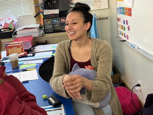 Woman smiling in a classroom holding a stuffed toy.