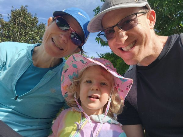 Family of three smiling outdoors on a sunny day.