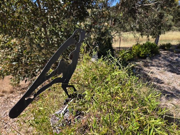 Metal bird silhouette garden decoration among greenery outdoors.