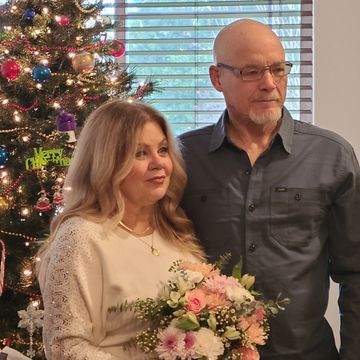 Couple standing near a decorated Christmas tree holding a bouquet of flowers.