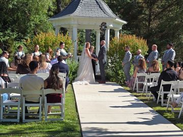 Outdoor wedding ceremony with bride and groom at the altar under a gazebo.