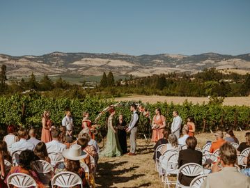 Outdoor wedding ceremony in a vineyard with mountains in the background.