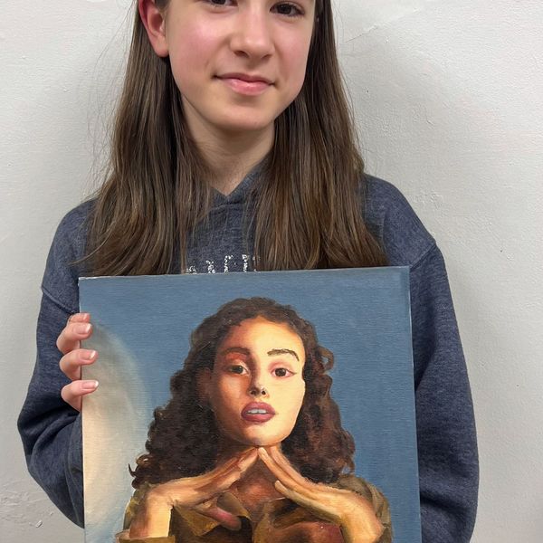 A girl proudly holding a painted portrait of a woman with curly hair.