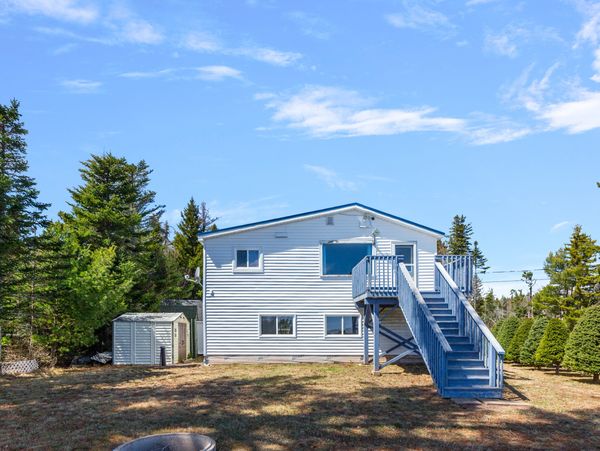 White two-story house with blue stairs and a spacious backyard under a clear sky.