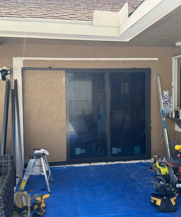 Sliding glass door installation in progress on a patio with tools and a blue tarp.