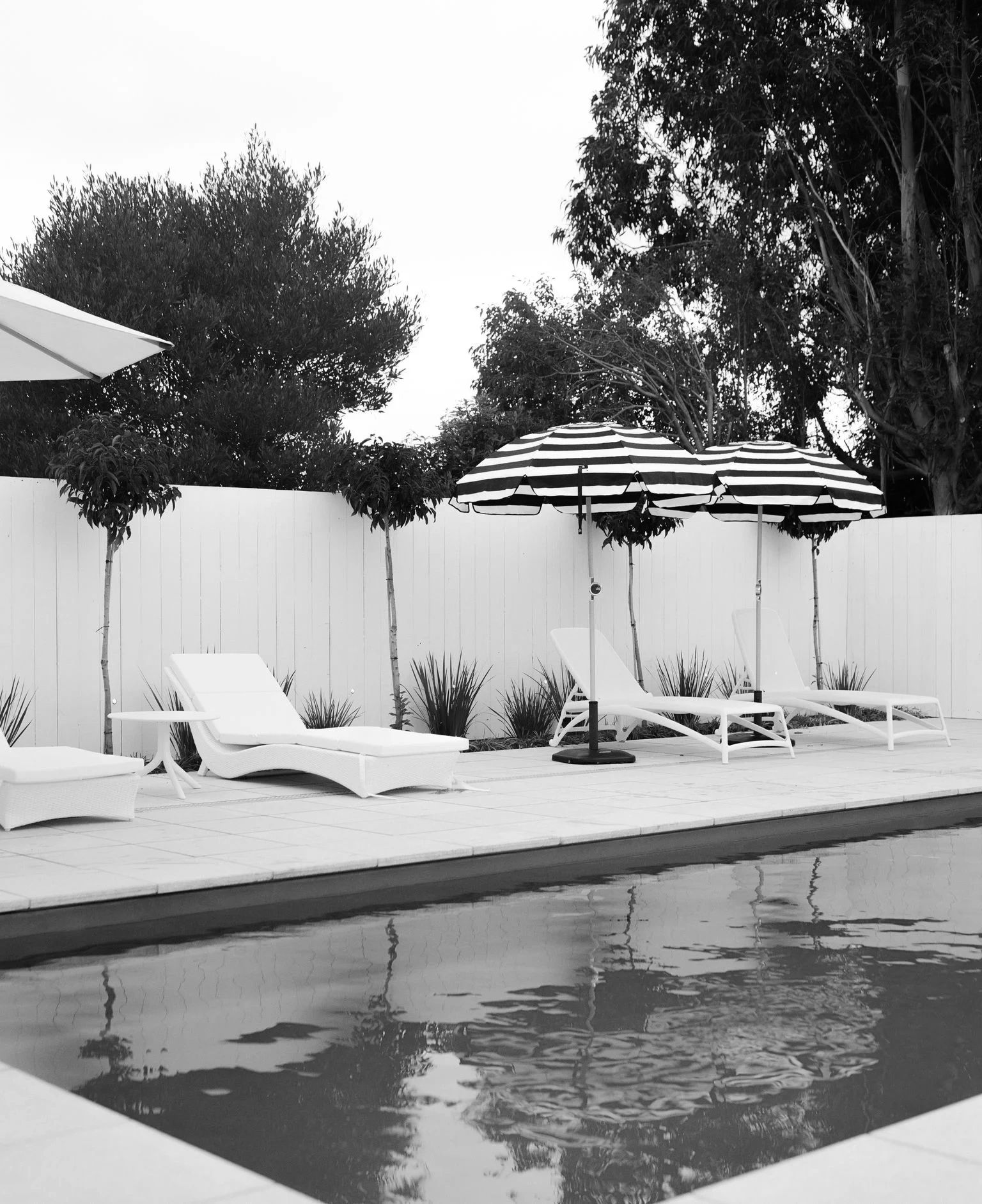 Modern poolside with white loungers and black-and-white striped umbrellas.