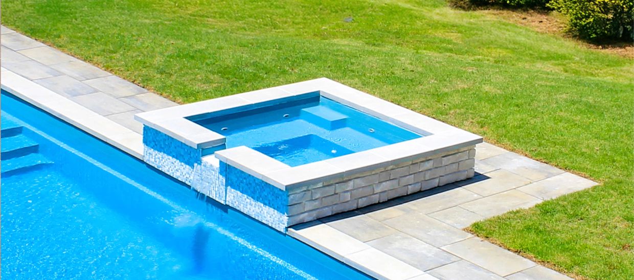 Blue pool and jacuzzi setup with stone edging and green lawn.