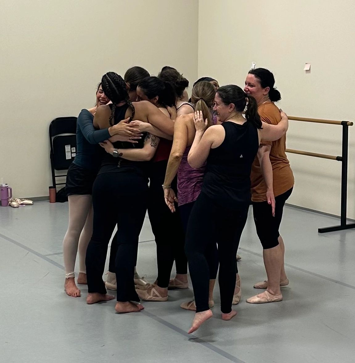 A group hug among ballet dancers in a studio.