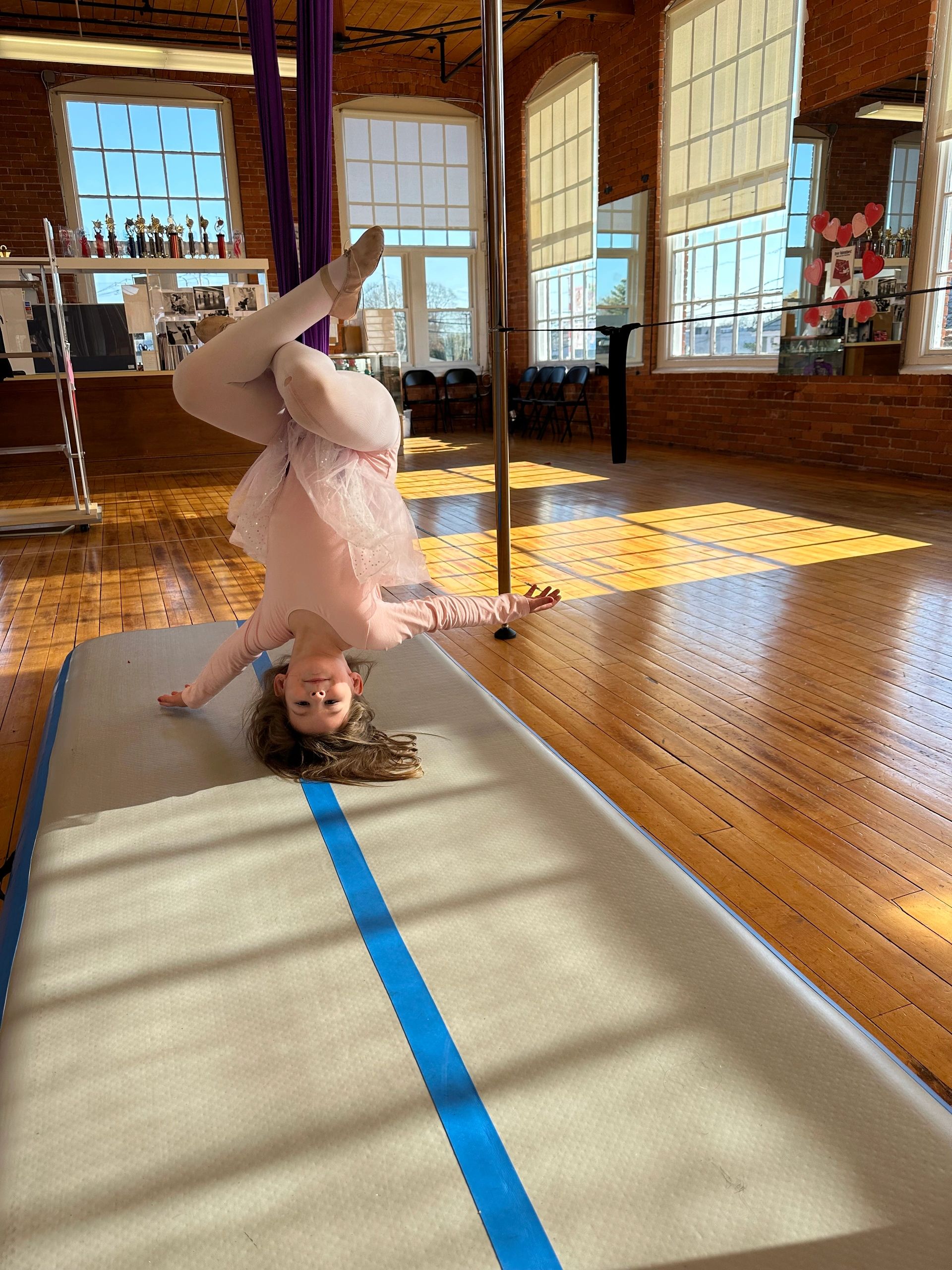 Young ballerina in pink tights balancing upside down in a sunlit dance studio.