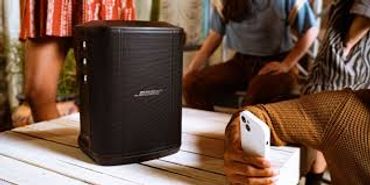 A Bose speaker on a table with people around.