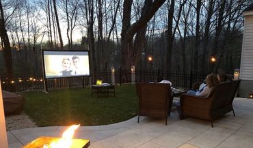 People watching an outdoor movie at dusk with a fire pit nearby.