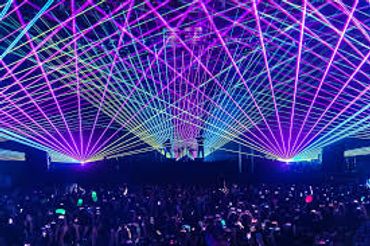 Colorful laser lights illuminate a large crowd at a concert or festival.